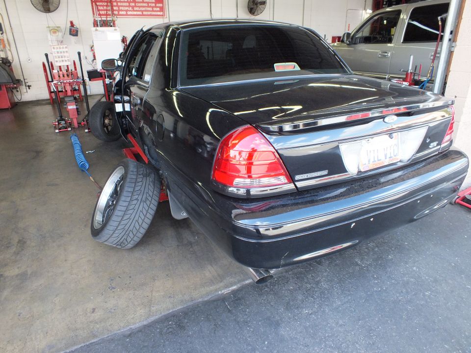 Black Ford Crown Victoria rear three-quarter on a shop lift, spare wheel leaning on bumper