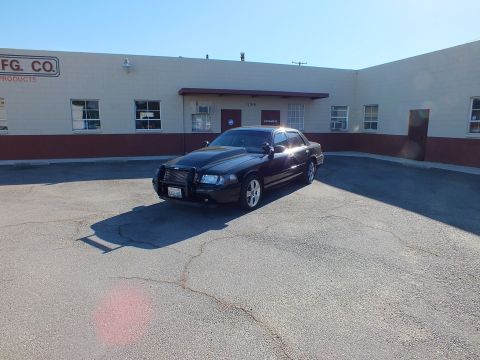 2003 Ford Crown Victoria - Distant front-left view of the black Crown Victoria parked in front of a warehouse marked Mfg. Co.