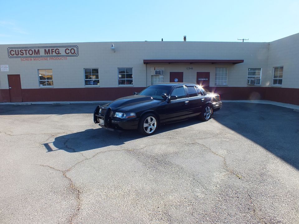 Black Ford Crown Victoria parked before Custom Mfg. Co. screw machine products building