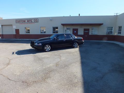 2003 Ford Crown Victoria - Wide shot of the black Crown Victoria angled across a cracked asphalt lot near Custom Mfg. Co.
