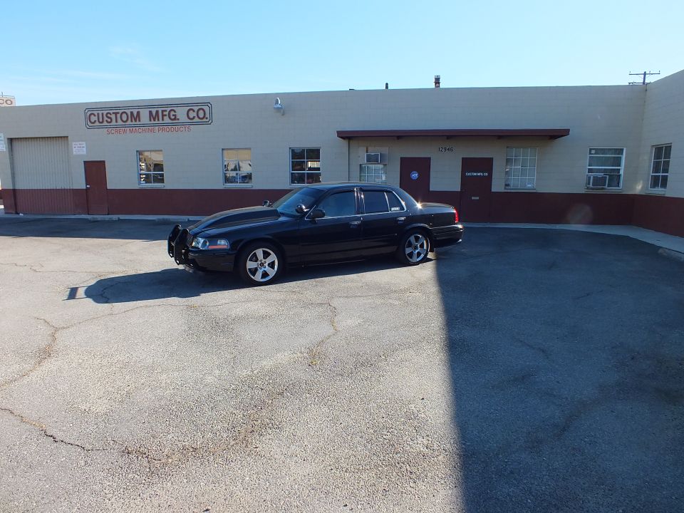 Black Ford sedan with push bar parked diagonally in lot at Custom Mfg. Co.