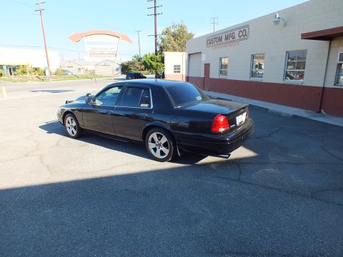 2003 Ford Crown Victoria - Rear-left view showing the black sedan's trunk, taillights and polished wheels in a lot.