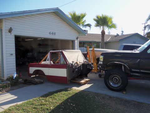 1968 Ford Bronco - A red and white 1968 Ford Bronco body sits disassembled in a driveway, with a black truck parked nearby.