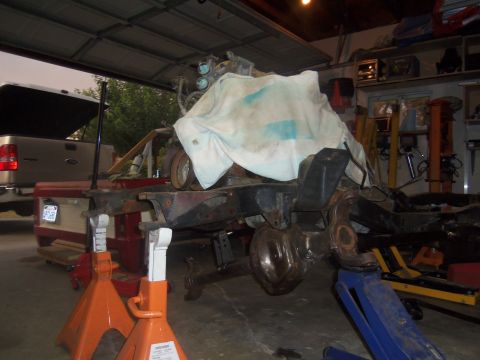 1968 Ford Bronco - The chassis and engine of a vehicle are undergoing work in a garage, with a pickup truck parked nearby.