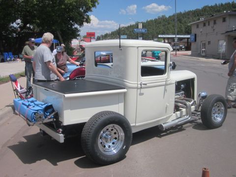 1991 Ford LTD Crown Victoria - A cream-colored hot rod pickup truck with a custom bed and exposed engine is displayed at an outdoor car show.