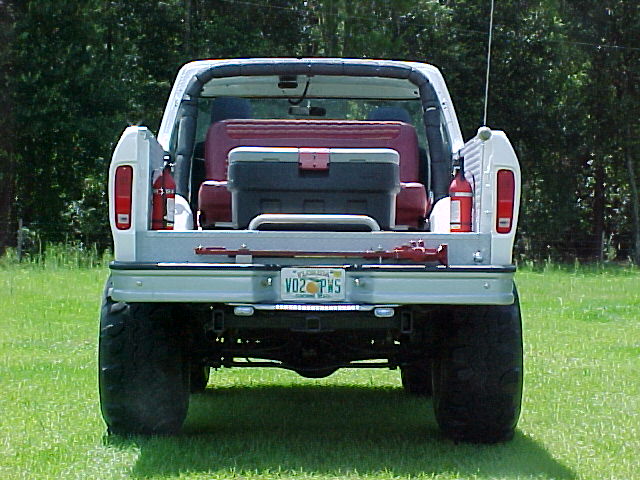 White lifted Ford Bronco rear view, red bench seat, fire extinguishers, high-lift jack on tailgate