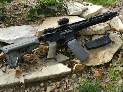 1996 Ford Bronco - An assault rifle with an extended magazine and optic is placed on a bed of rocks and fallen leaves.