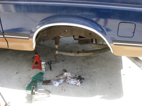 1994 Ford Bronco - The rear axle and suspension of a vehicle are visible, with tools laid out on the ground for maintenance.