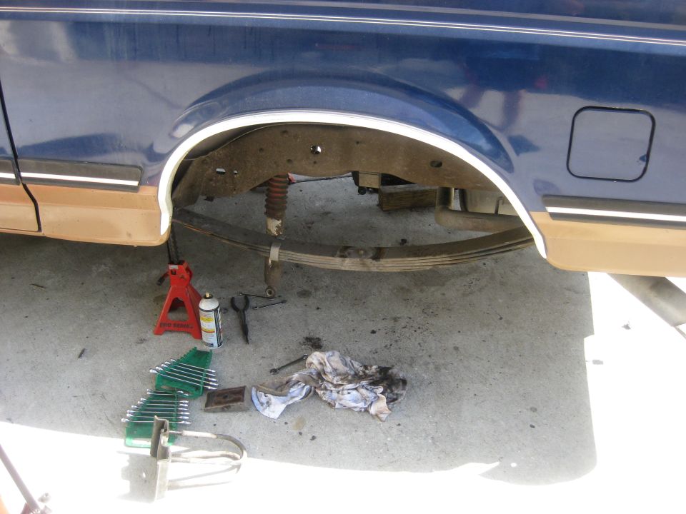 vehicle's rear suspension with leaf springs and shock absorber, tools and jack stands on the ground