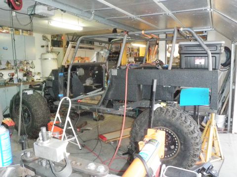 1961 International Scout 800 - A custom off-road vehicle is in progress, a prominent roll cage and large tires within a workshop setting.