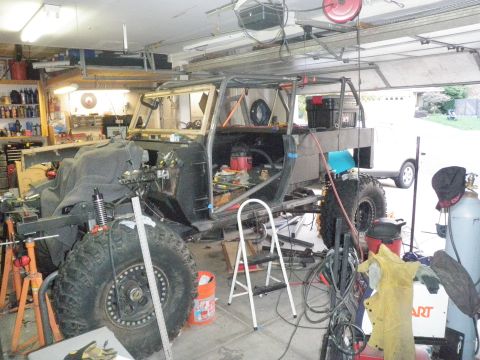 1961 International Scout 800 - Custom off-road vehicle build in progress inside a garage with tools and equipment visible.