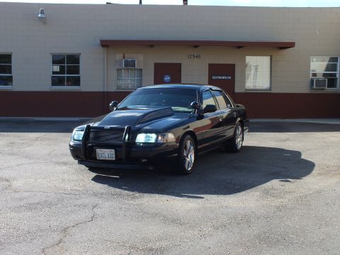 2003 Ford Crown Victoria - Front-left angle of the black sedan showing hood scoop, push bar and chrome wheels.