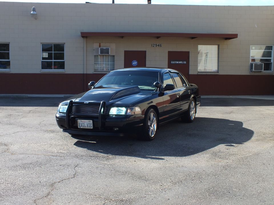 Front three-quarter of black Crown Victoria with push bar and hood scoop in lot