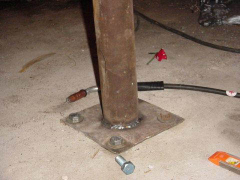 1992 Ford Bronco - A welding torch is positioned near the base of a metal pole, which is secured to the floor with bolts.