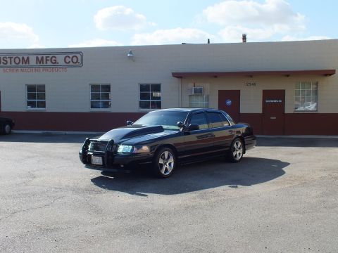 2003 Ford Crown Victoria - Front-left view of the black sedan with hood scoop and chrome wheels in a paved lot.
