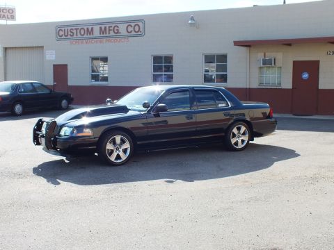 2003 Ford Crown Victoria - Front-left view of the modified black sedan on cracked asphalt by an industrial unit.
