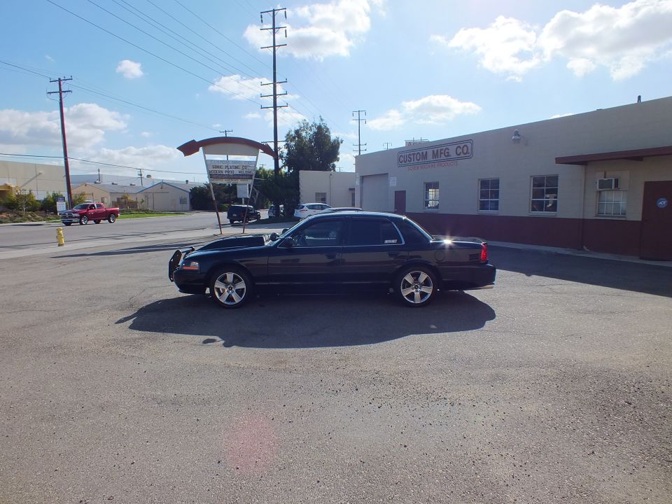 Side profile of black Ford sedan with push bar and chrome wheels in parking lot