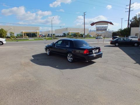 2003 Ford Crown Victoria - Rear-left view of the black Ford sedan with chrome wheels in a wide paved lot.