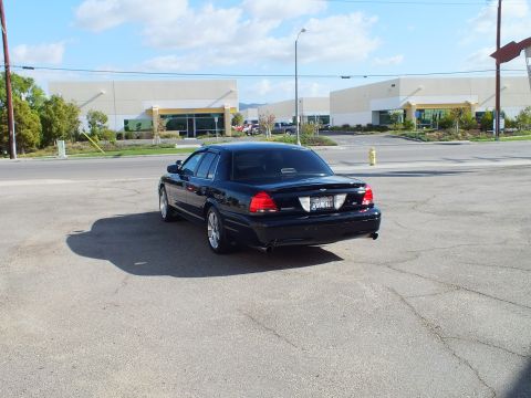 2003 Ford Crown Victoria - Rear-left angle of the black Ford showing taillights, dual exhaust and chrome wheels.