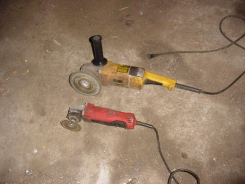 1992 Ford Bronco - Two angle grinders, one yellow and one red, lie on a concrete surface with their cords trailing.