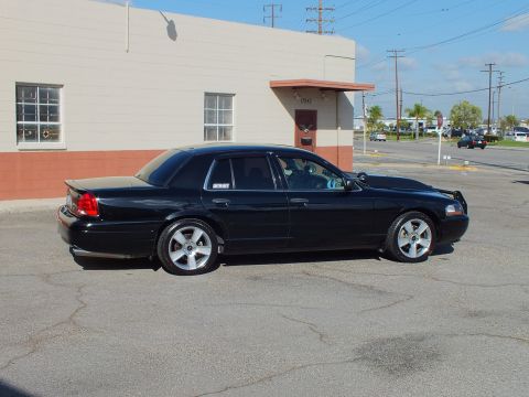 2003 Ford Crown Victoria - Side profile of a lowered black sedan with Marauder badge on quarter panel, parked beside a tan industrial building.