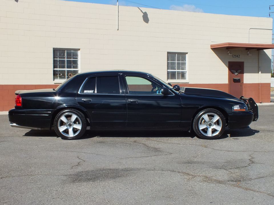 Black Mercury Marauder side profile in sunlight, polished wheels, lowered stance, tan building behind