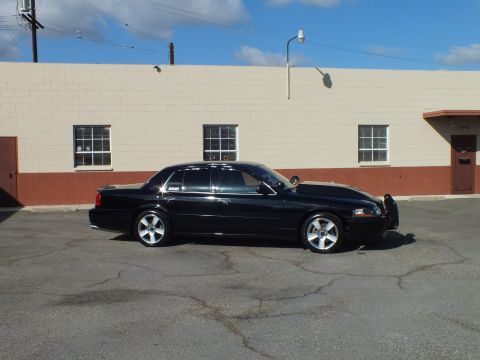 2003 Ford Crown Victoria - Black full-size sedan shot side-on in a wide cracked parking lot with overhead power lines.
