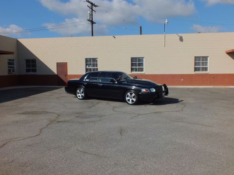 2003 Ford Crown Victoria - Front quarter of a lowered black sedan parked in a wide asphalt lot under a blue sky.