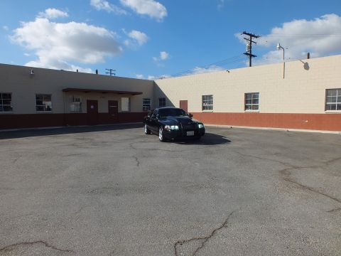 2003 Ford Crown Victoria - Wide shot of a black Mercury Marauder small in frame against industrial buildings and blue sky.
