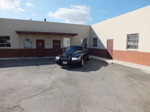 2003 Ford Crown Victoria - Black sedan parked near loading doors of a tan block building, headlights illuminated.