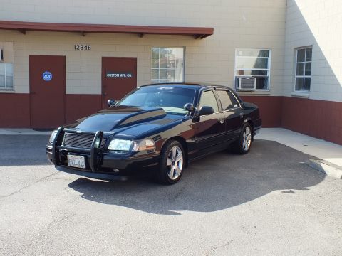 2003 Ford Crown Victoria - Front quarter of a black full-size sedan with brush guard and chrome wheels at a Custom Mfg Co dock.