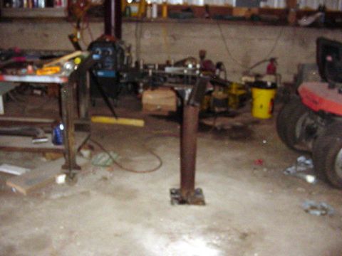 1992 Ford Bronco - A dim shop interior with heavy steel tube stands bolted to base plates on the concrete floor supporting a bare chassis or frame jig behind…