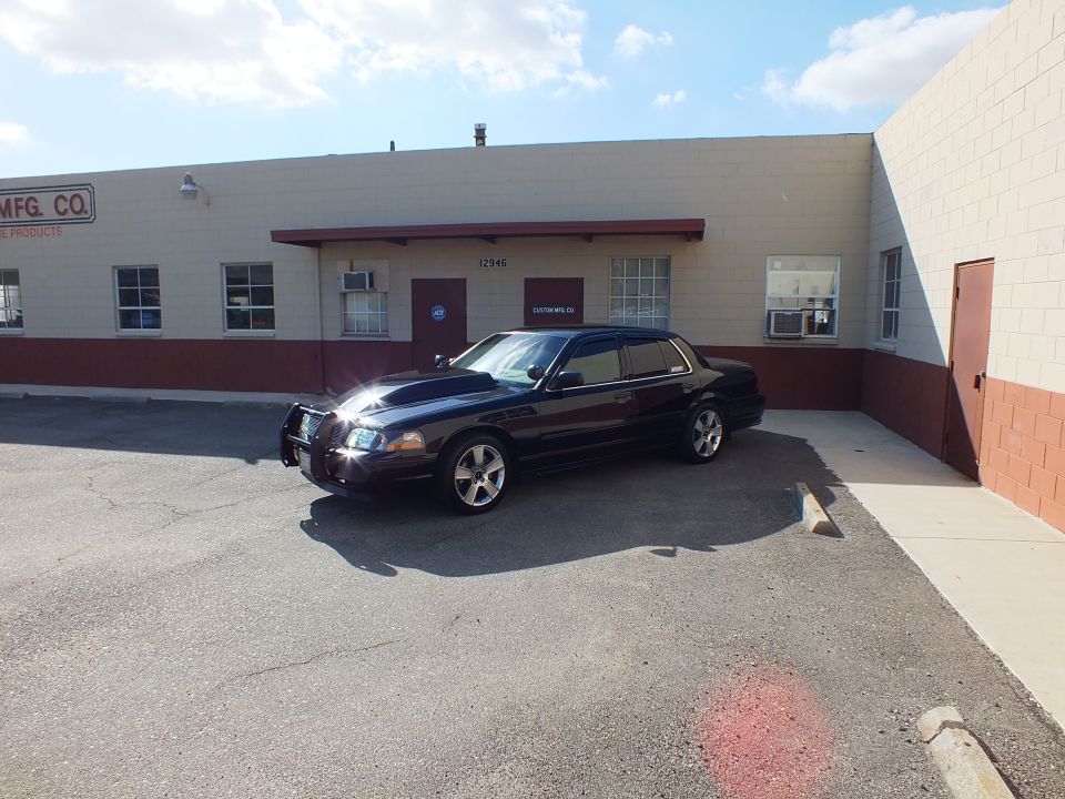 Black Mercury Marauder front quarter with chrome push bar, MFG CO sign on tan warehouse behind