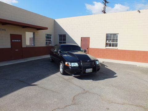 2003 Ford Crown Victoria - Black full-size sedan with brush guard parked in lot, hood and roof catching afternoon sun.