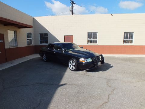 2003 Ford Crown Victoria - Black sedan fitted with brush guard and chrome wheels parked at angle in industrial lot.