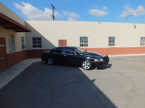 2003 Ford Crown Victoria - Side profile of a lowered black full-size sedan with chrome wheels in an industrial parking lot.