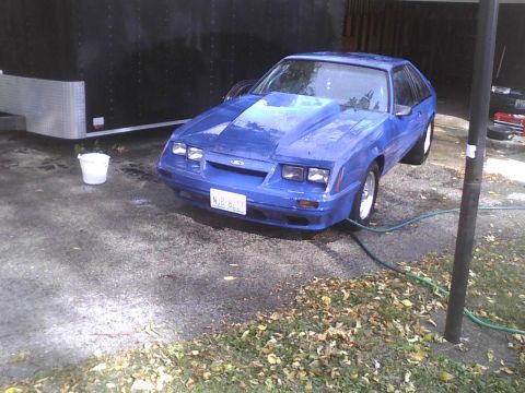 2003 Ford Crown Victoria - A blue Ford Mustang hatchback with a prominent hood scoop is parked outdoors near a trailer.