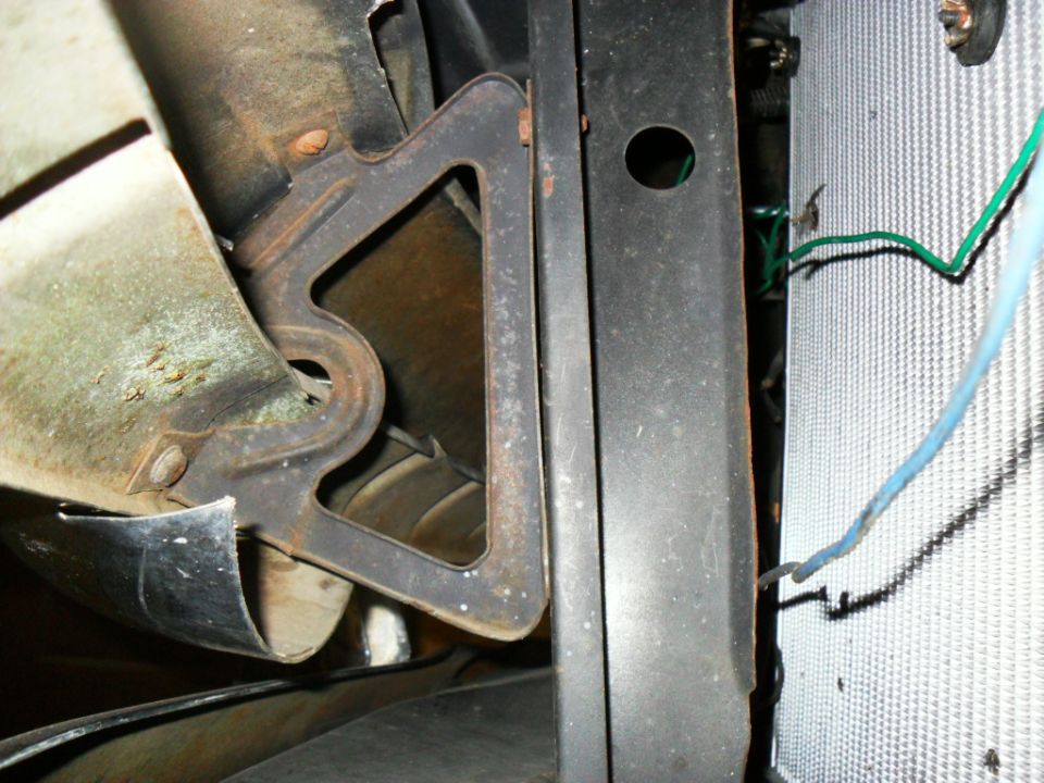 Rusty triangular metal bracket near black support and radiator core with colored wiring