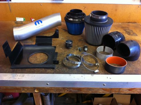 2010 Dodge Challenger - Various automotive intake components are laid out on a wooden workbench, including a Mopar branded tube and two air filters.