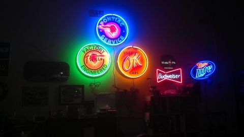 1973 Chevrolet Camaro - A wall displays several vintage neon signs, advertising brands like Pontiac, Budweiser, and Miller Lite, along with general service and sal…