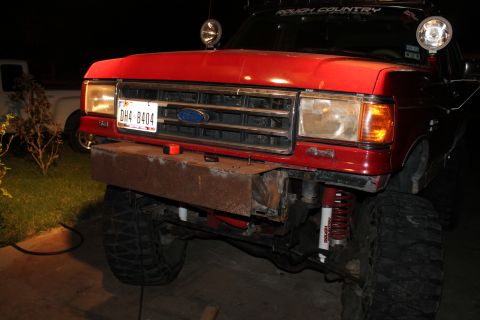 1990 Ford Bronco - Front view of a red Ford truck with a custom bumper and off-road suspension components.