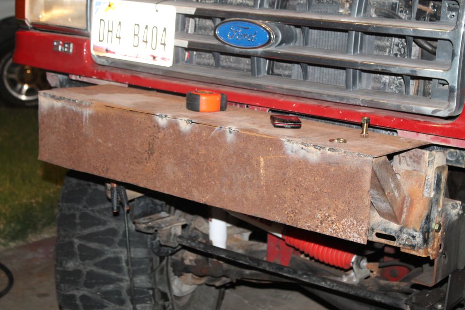 Custom rusty bumper on red truck front, Ford emblem visible