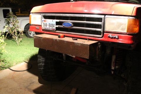 1990 Ford Bronco - A red Ford truck is shown with a custom-built metal bumper and a license plate. Another truck is visible in the background.