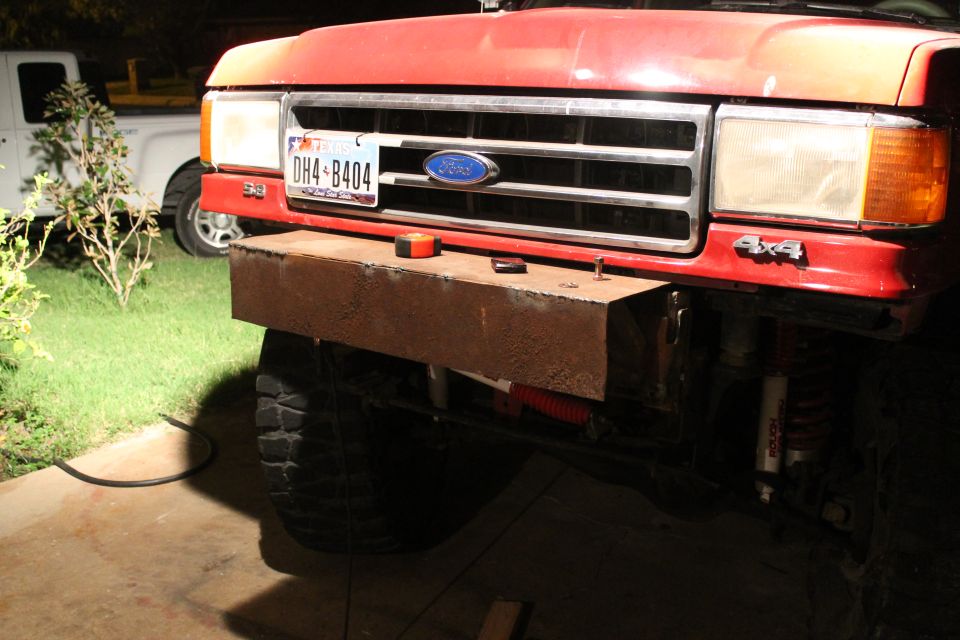 Red Ford truck front end with a custom metal bumper and a license plate DH4-B404. White truck in background