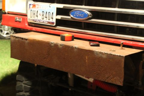 1990 Ford Bronco - A close-up of a red Ford truck's front end reveals a custom, rusty bumper and a Texas license plate.