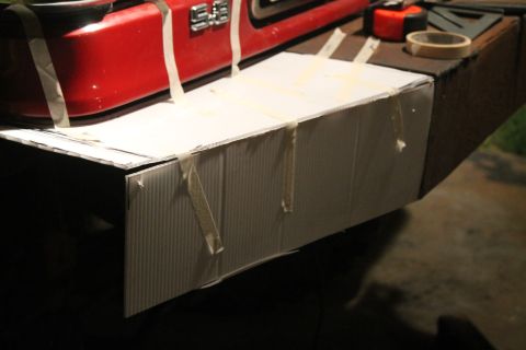 1990 Ford Bronco - A red bumper section with an "S.E." badge is taped to a cardboard extension, with tools nearby.