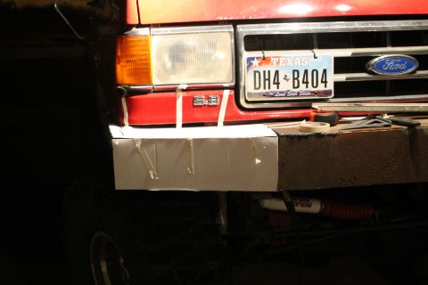 1990 Ford Bronco - A red 1990 Ford Bronco features a temporary cardboard bumper cover over its front end, with a Texas license plate visible.
