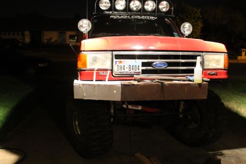 1990 Ford Bronco - This red Ford truck features a custom bumper and roof-mounted lights, with a license plate reading DH4-8404.