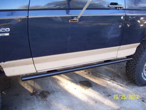 1990 Ford Bronco - The side of a blue and tan Ford Bronco is visible, with a running board and tire in view.