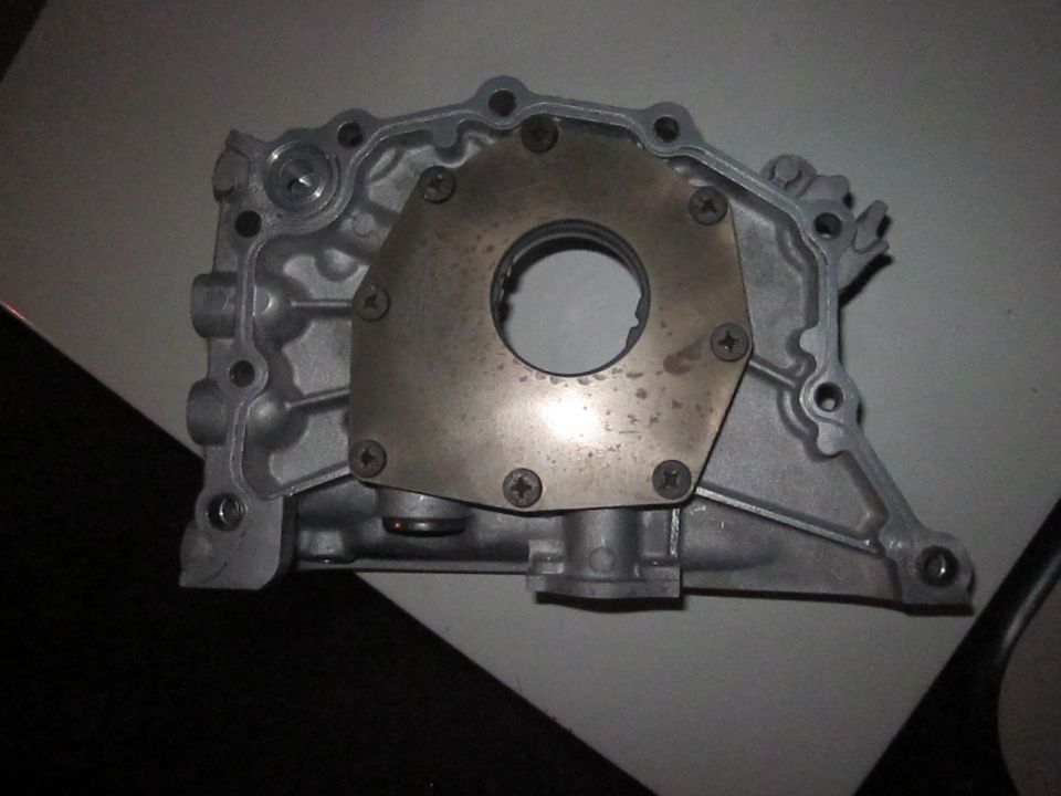 Close-up of an aluminum oil pump housing with a metal plate secured by screws